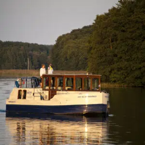 Kormoran fährt im Herbst über einen ruhigen See, an Bord ein Paar