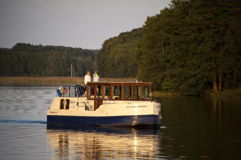 Kormoran fährt im Herbst über einen ruhigen See, an Bord ein Paar