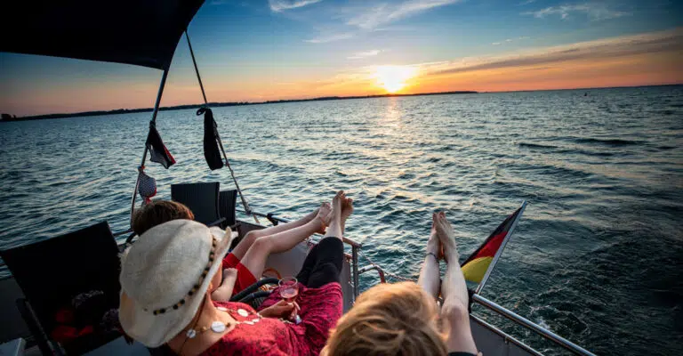 Drei Frauen an Deck einer Babro Beluga. Sie haben die Beine an der Reling hochgelegt und schauen zum Sonnenuntergang.