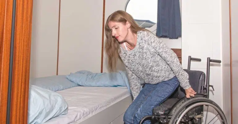 Eine Rollstuhlfahrerin steht von ihrem Rollstuhl auf um sich ins Bett zu legen.
