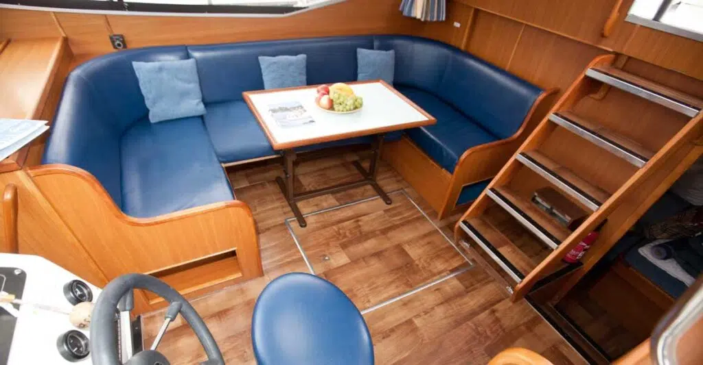 Ein Salon mit einer blau gepolsterten Sitzecke und einem kleinen Tisch in der Mitte. Daneben befindet sich die Treppe zum Sonnendeck.