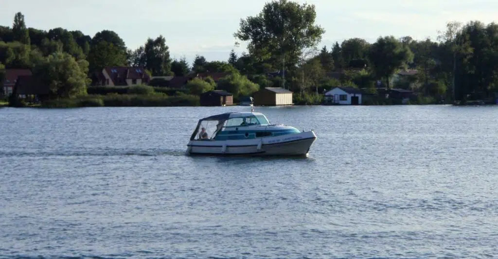 die Bellus fährt über einen See, im Hintergrund sind Bootshäuser