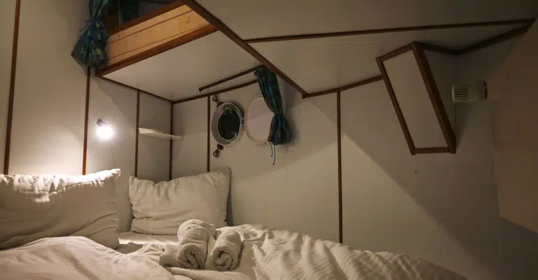 Eine Kabine im Bug der Kormoran mit einem Doppelbett.. Das Bett ist mit weiß gestreiften Bezügen bezogen.