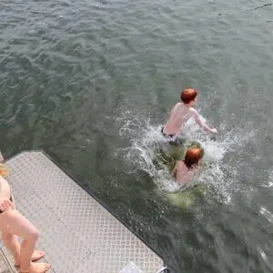 Zwei Personen stehen auf der Badeplattform einer Kormoran. Zwei weitere Leute sind bereits ins Wasser gesprungen.