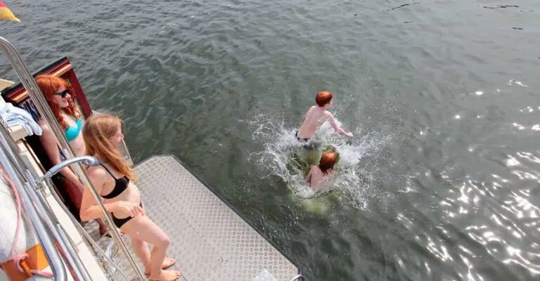 Zwei Personen stehen auf der Badeplattform einer Kormoran. Zwei weitere Leute sind bereits ins Wasser gesprungen.