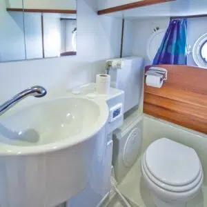 Badezimmer einer Kormoran im Bug mit Toilette und Waschbecken mit beweglichem Duschkopf. Die Toilette kann mit einer Platte in Holzoptik abgedeckt werden.