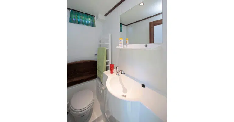 Das Badezimmer der Aquino 1190 D mit Toilette und Waschbecken mit beweglichem Duschkopf. Die Toilette Kann abgedeckt werden mit einer Platte in Holzoptik.