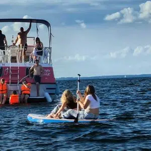Zwei Mädchen auf einem SUP Paddeln zur Pirate. Auf der Badeplattform sind drei Personen. Eine Person ist im Wasser. Drei Personen befinden sich auf dem Sonnendeck.