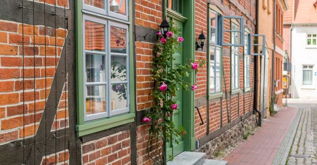 Ein rotes Fachwerkhaus mit grünen Fensterrahmen und einer Grünen Tür sowie Rosen neben der Tür.