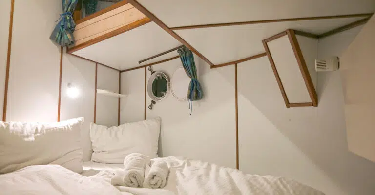 Eine Kabine im Bug der Kormoran mit einem Doppelbett.. Das Bett ist mit weiß gestreiften Bezügen bezogen.