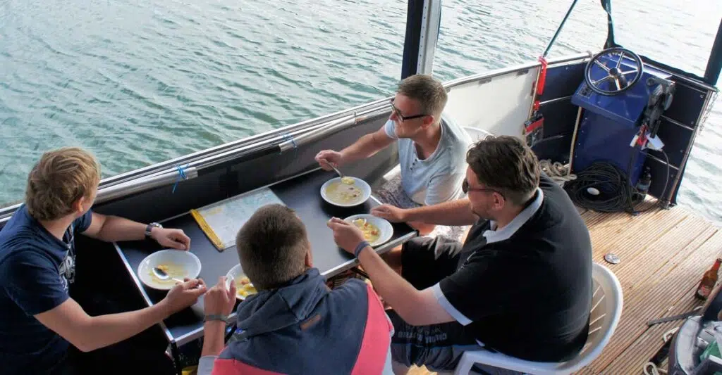Vier männer sitzen an bord eines febo 720 open und essen suppe