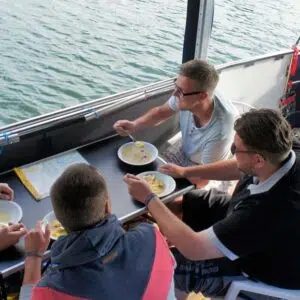 Vier männer sitzen an bord eines febo 720 open und essen suppe