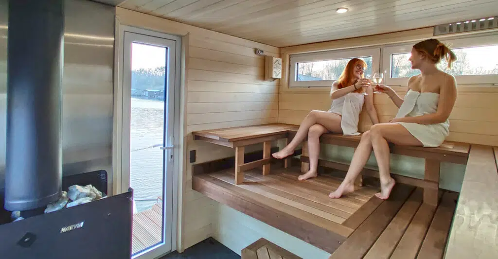 Zwei junge Frauen im Saunabereich des Saunahausbootes stoßen auf ein Glass Weißwein an.