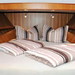 Bugkabine mit Doppelbett. Kissen und Decken sind mit weiß-beige-braun gestreiften Bezügen bezogen.