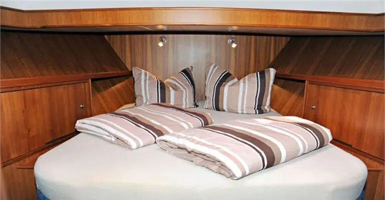 Bugkabine mit Doppelbett. Kissen und Decken sind mit weiß-beige-braun gestreiften Bezügen bezogen.