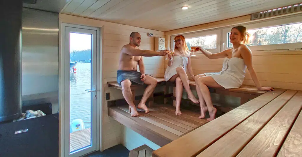 Drei Personen im Saunabereich des Saunahausbootes stoßen auf ein Glas Champagner an.