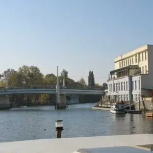 Eine Kormoran auf einem Kanal in Brandenburg mit Blick auf ein Restaurant und einer Brücke.