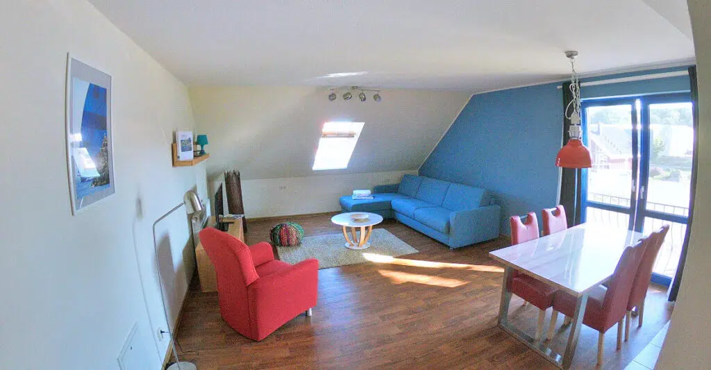 Wohnzimmer mit Couch, Sessel und Esstisch mit Tür zum Balkon.